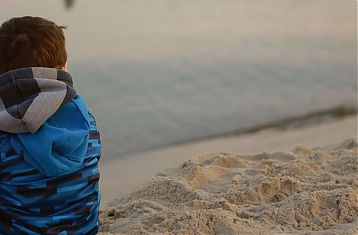 Jongetje met jas en sjaal op het strand op de rug gezien