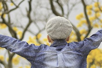 Jongen op de rug gezien met jeansshirt aan voor een boom met gele bladeren