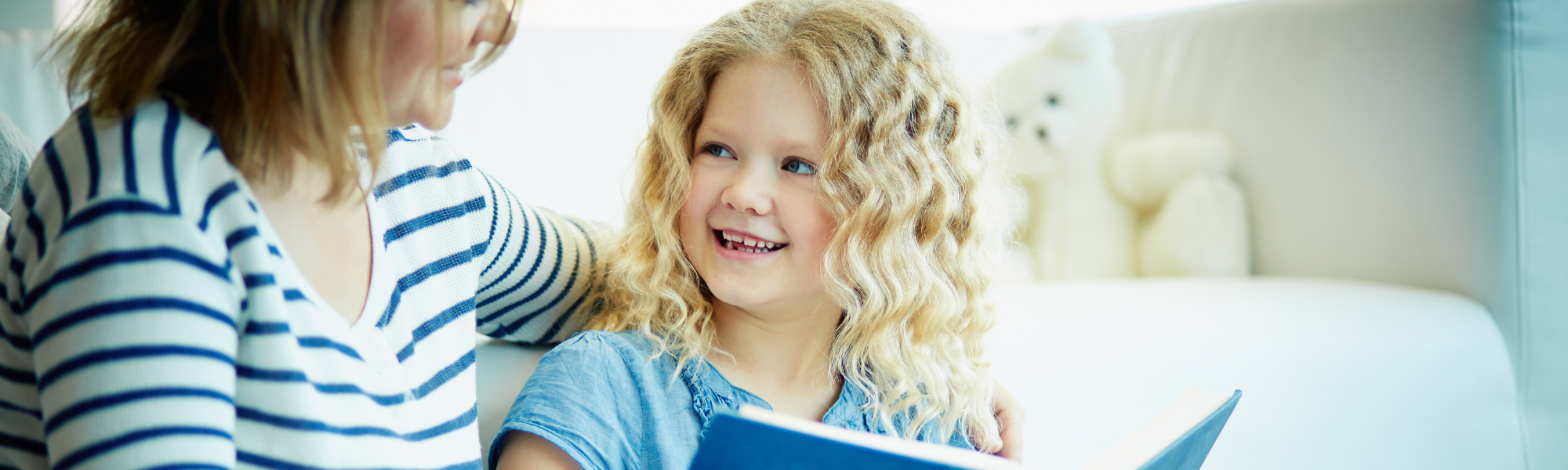 Kind met open boek in handen kijkt lachend opzij naar volwassene – moment van contact, plezier en gedeeld leerproces.