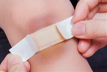 Handen plakken een pleister op de bezeerde knie van een kind.